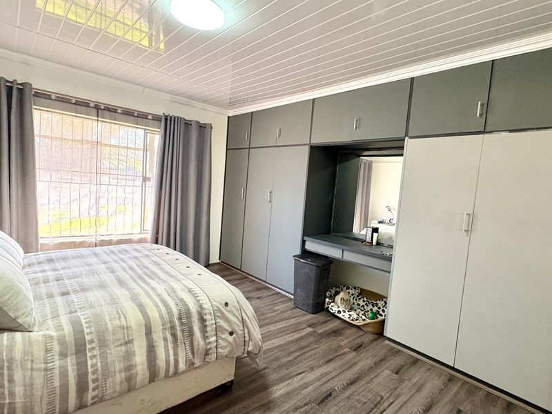 A well-maintained bedroom featuring extensive built-in cupboards with an integrated vanity, modern laminate flooring, and a clean PVC ceiling finish.