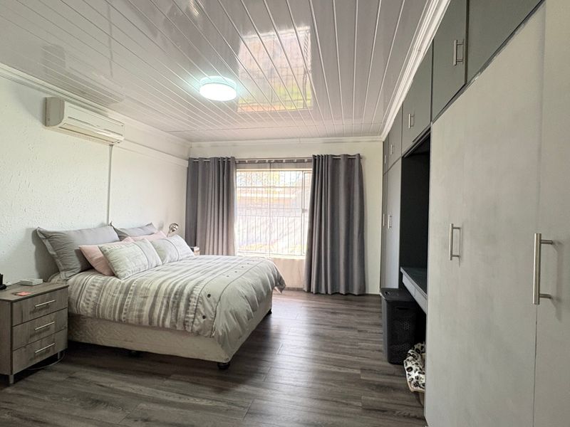 Spacious bedroom featuring laminate flooring, built-in cupboards, an air conditioning unit, and a modern PVC ceiling finish.