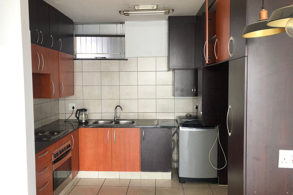 A functional kitchen featuring built-in cabinetry, a double sink, electric oven, and hob, with tiled splashbacks and flooring throughout.