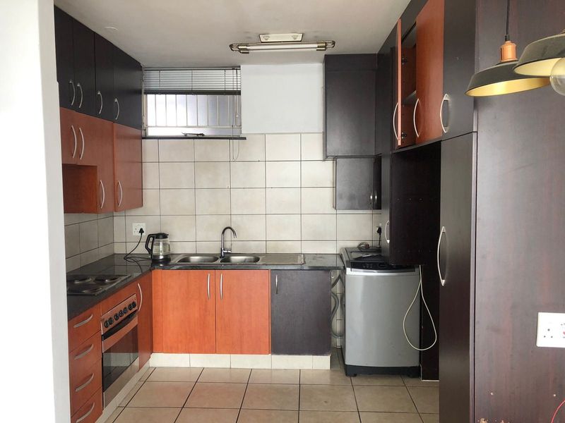 A functional kitchen featuring built-in cabinetry, a double sink, electric oven, and hob, with tiled splashbacks and flooring throughout.