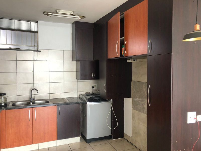 A compact kitchen featuring dark and wood-tone cabinetry, a double bowl sink, and tiled splashbacks, currently requiring some maintenance and cosmetic updates.