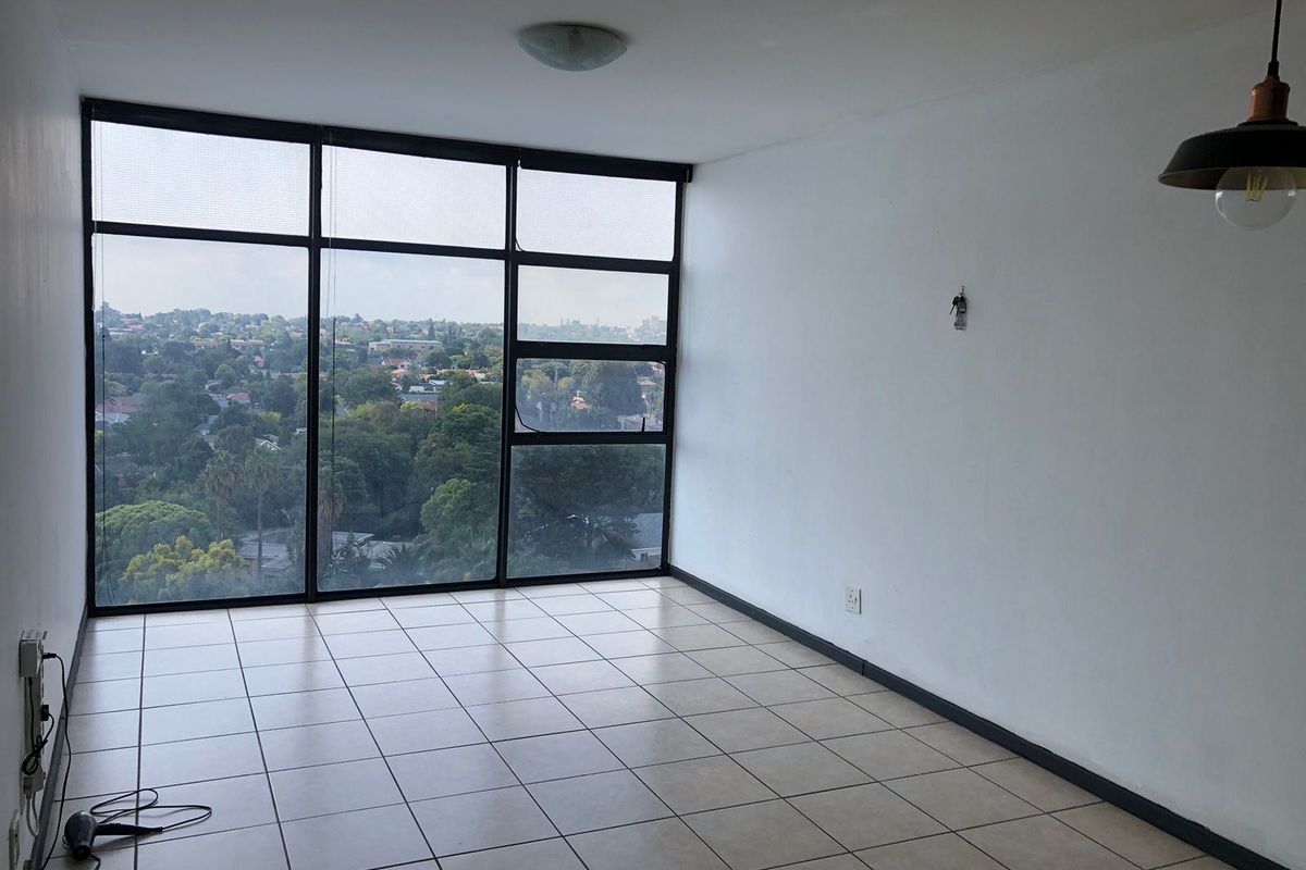 An empty, sunlit living area featuring large floor-to-ceiling windows with expansive views, ceramic tiled flooring, and modern pendant lighting.