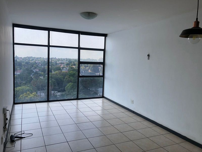 An empty, sunlit living area featuring large floor-to-ceiling windows with expansive views, ceramic tiled flooring, and modern pendant lighting.