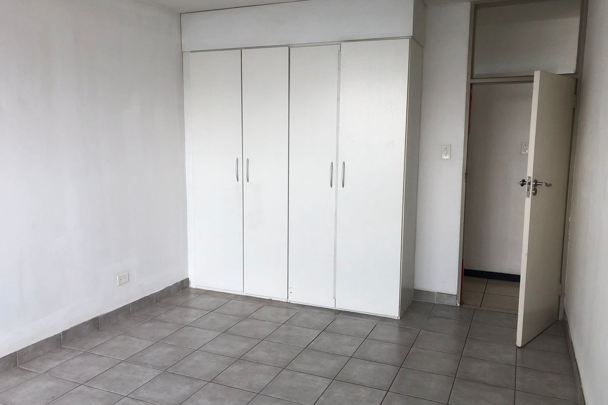 A vacant bedroom featuring neutral tiled flooring and white built-in cupboards, offering a clean, blank canvas for personalization.