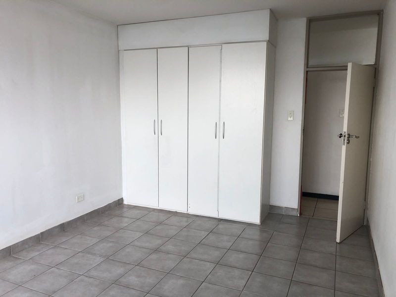 A vacant bedroom featuring neutral tiled flooring and white built-in cupboards, offering a clean, blank canvas for personalization.