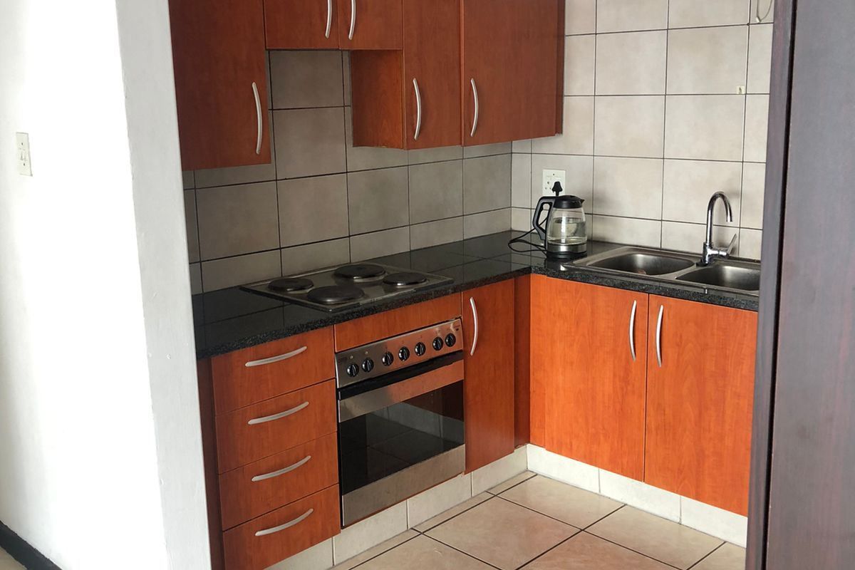 Compact kitchen featuring wooden cabinetry, dark countertops, built-in oven and hob, double sink, and tiled flooring.