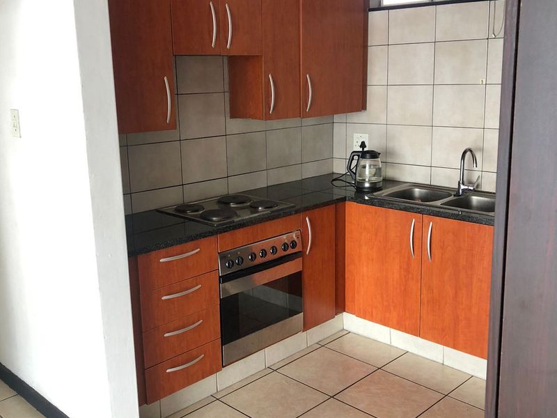 Compact kitchen featuring wooden cabinetry, dark countertops, built-in oven and hob, double sink, and tiled flooring.