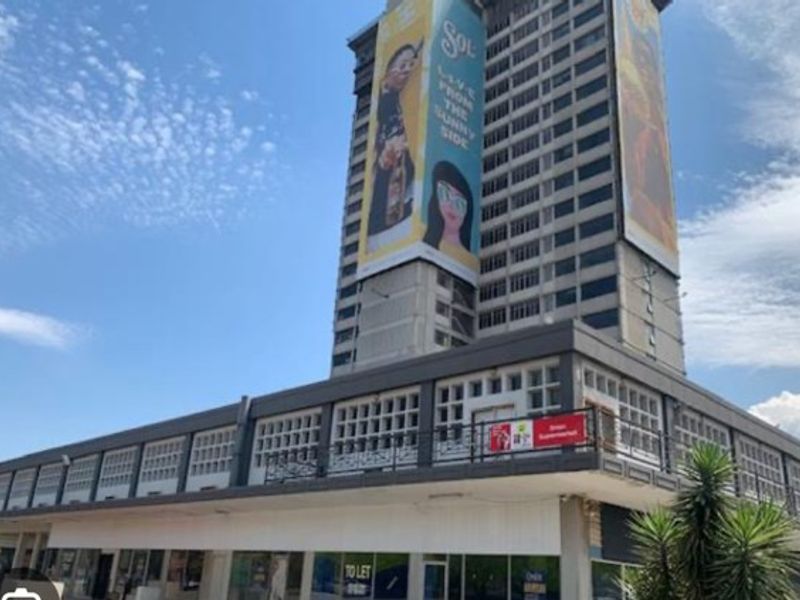 Exterior view of a multi-story apartment building featuring ground-level commercial storefronts and large advertising billboards on the facade.
