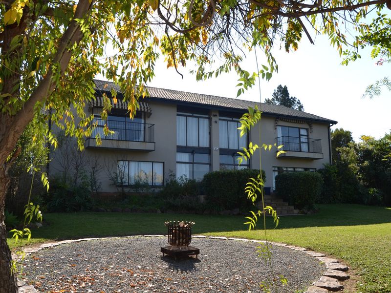 A spacious rear view of the two-story house featuring large glass sliding doors, upper-level balconies, and a well-maintained garden with a stone fire pit.