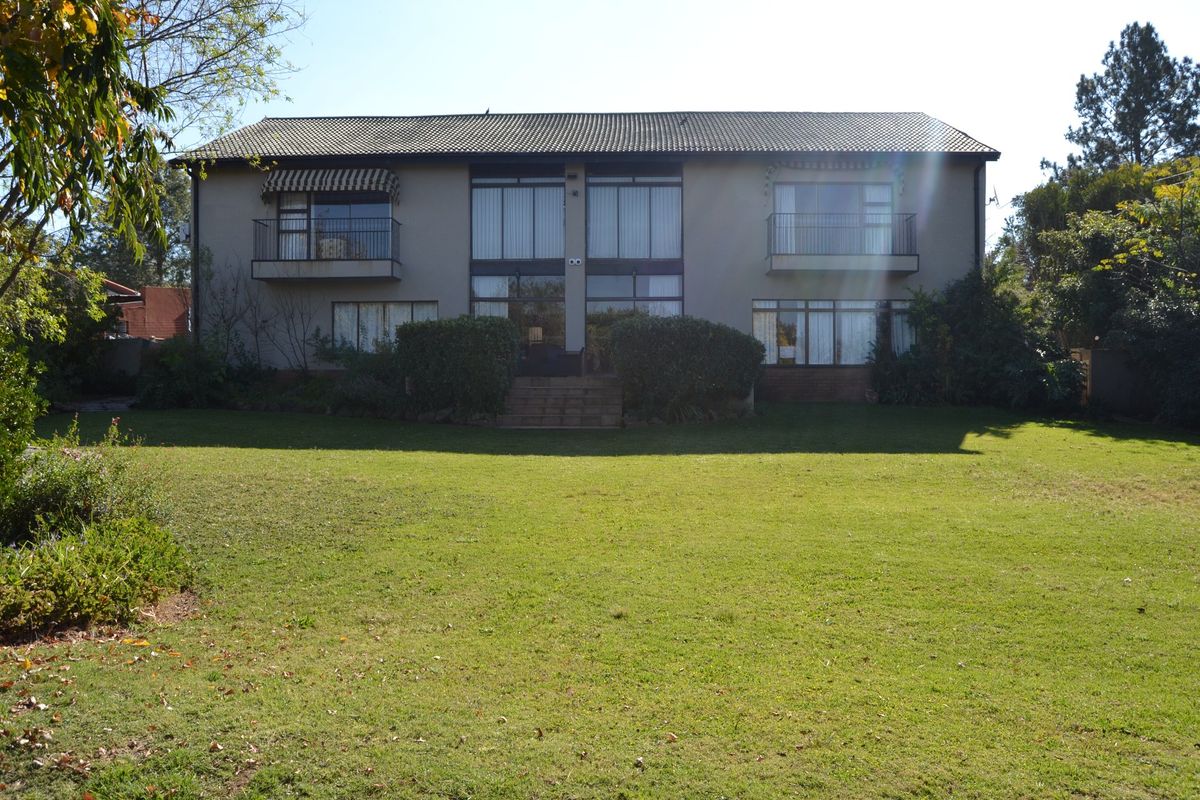 Rear view of a two-story residential house featuring a large lawn, upper-level balconies, and expansive windows providing natural light.