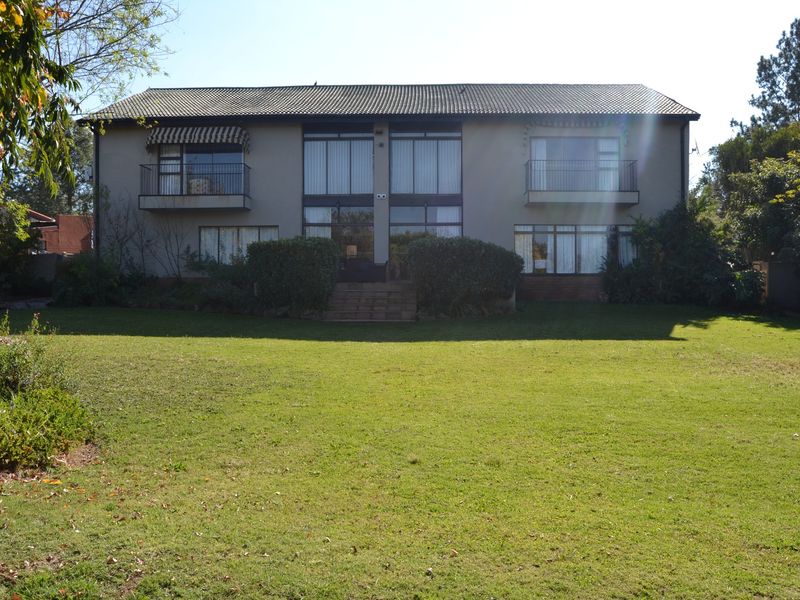 Rear view of a two-story residential house featuring a large lawn, upper-level balconies, and expansive windows providing natural light.