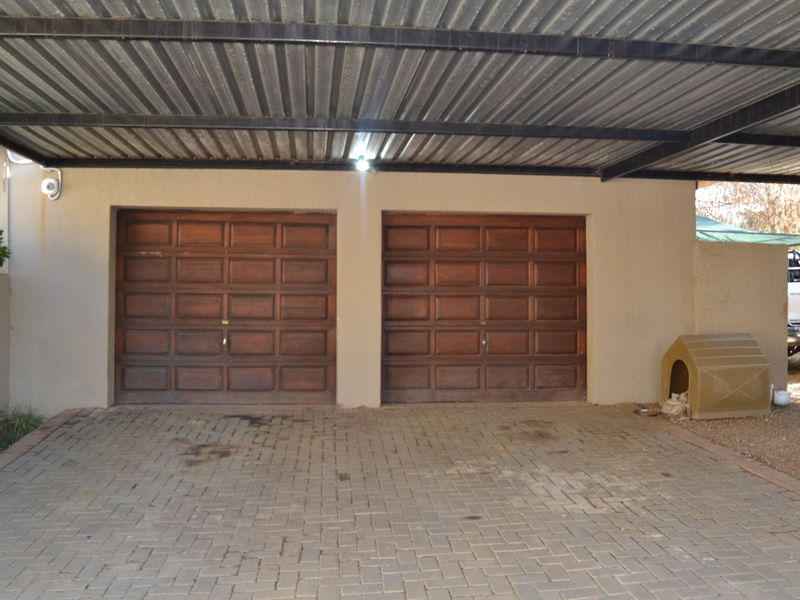 A double garage featuring wooden sectional doors and a covered carport area with paved flooring.