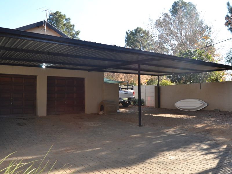 A paved driveway area featuring a double garage and an attached metal carport structure.