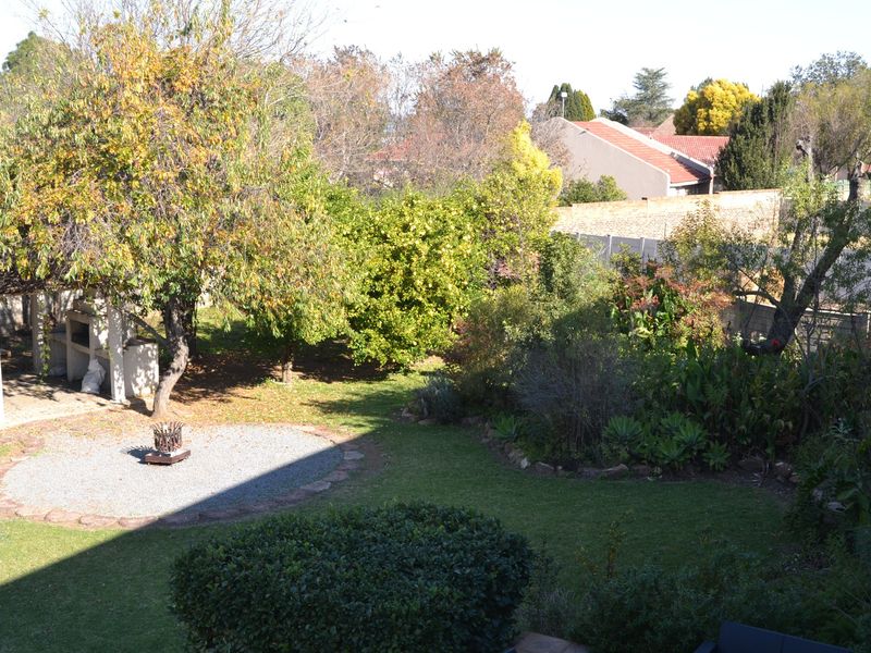 A spacious rear garden featuring a lawn, mature trees, a gravel seating area, and a built-in outdoor braai facility.