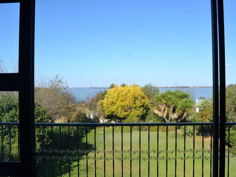 A scenic view of the garden and distant lake captured from an elevated balcony with a metal balustrade.
