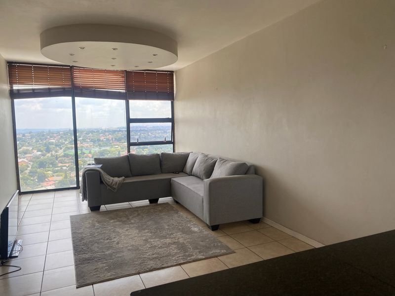 A bright living room featuring large floor-to-ceiling windows with expansive views, tiled flooring, and a unique circular recessed ceiling detail.