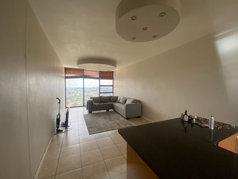 Open-plan living area featuring tiled floors, large windows with panoramic views, and a granite-topped kitchen counter, offering a bright and functional space.