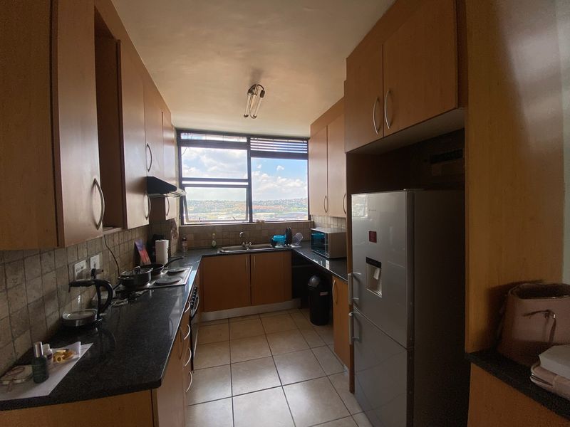 A functional galley-style kitchen featuring laminate cabinetry, granite countertops, and a built-in hob, offering a practical layout with natural light and city views.
