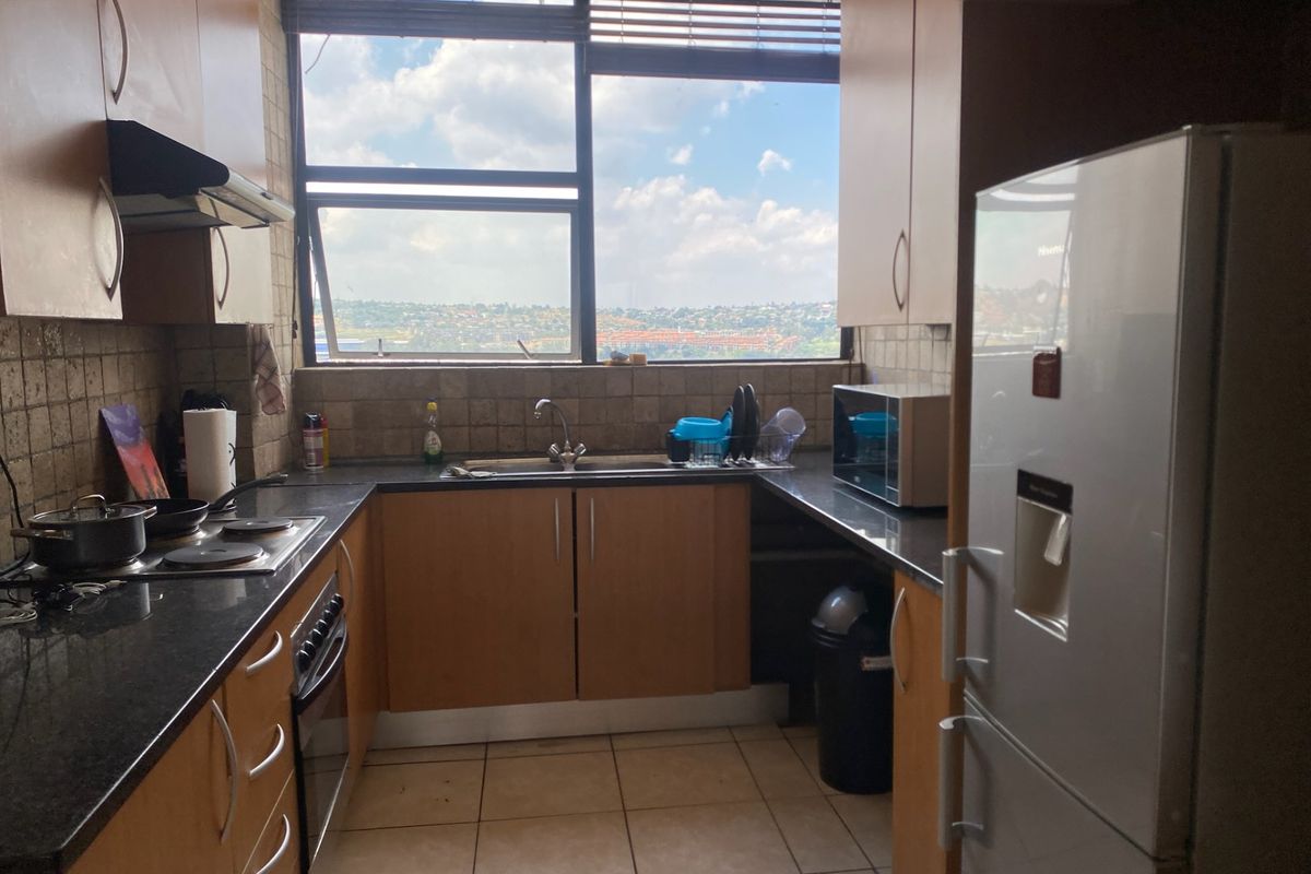 A functional kitchen featuring laminate cabinetry, granite countertops, built-in oven, electric hob, and a large window providing natural light and urban views.