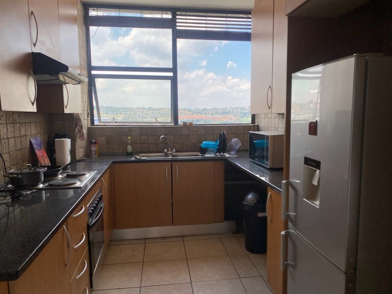 A functional kitchen featuring laminate cabinetry, granite countertops, built-in oven, electric hob, and a large window providing natural light and urban views.
