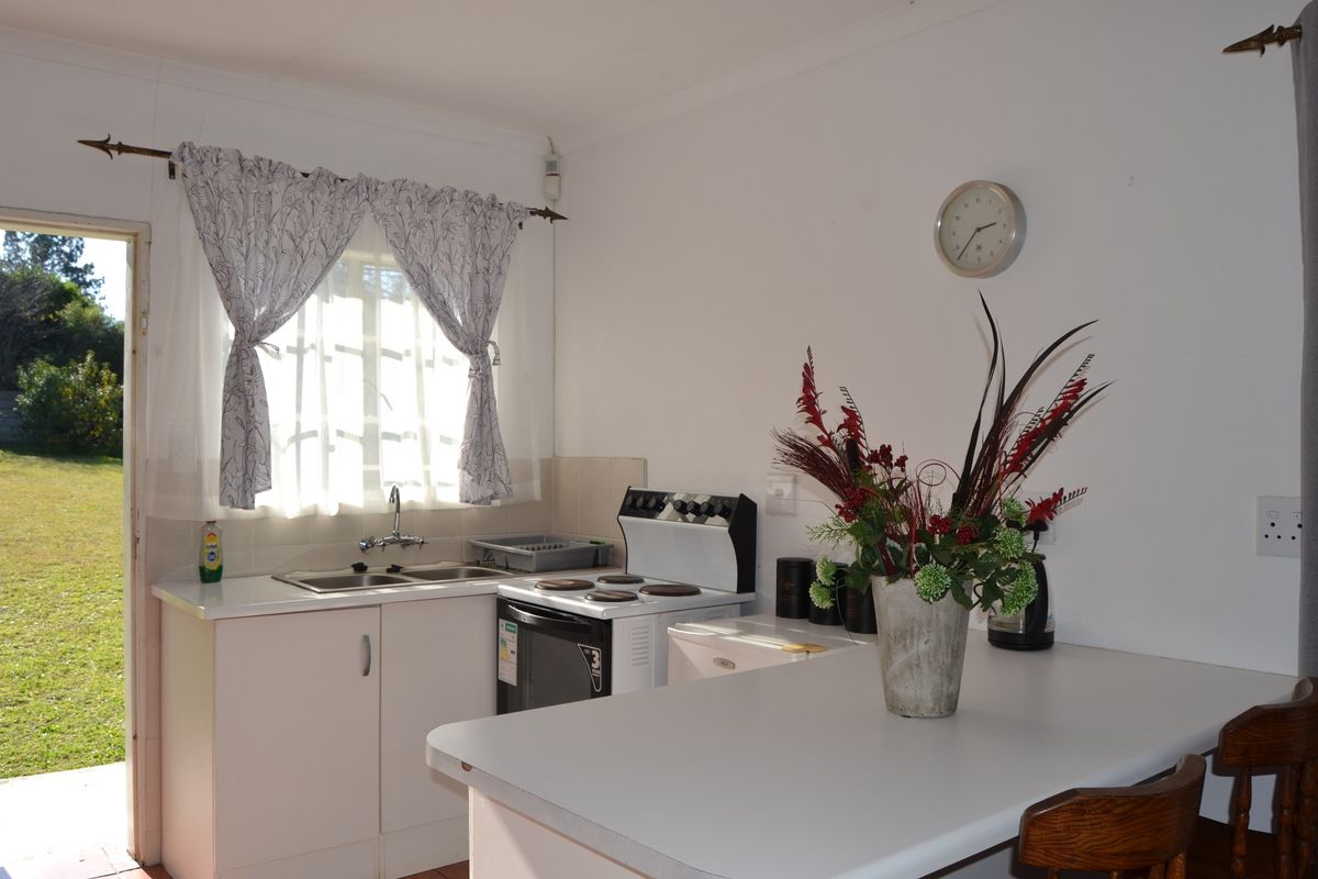 A functional kitchen featuring white cabinetry, laminate countertops, a double sink, and an electric stove, with direct access to the garden.