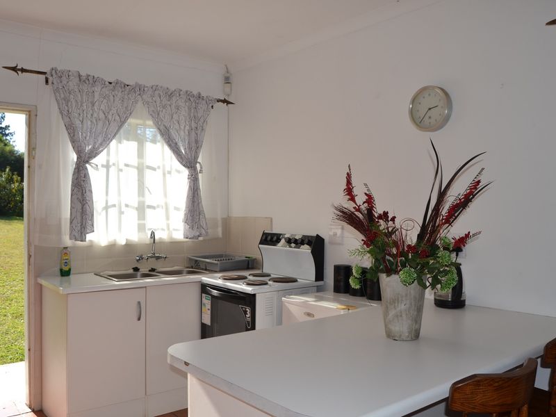 A functional kitchen featuring white cabinetry, laminate countertops, a double sink, and an electric stove, with direct access to the garden.