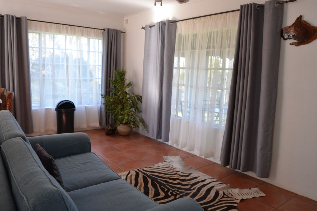 A bright living room featuring terracotta floor tiles and large windows with curtains, offering a comfortable and well-lit space.