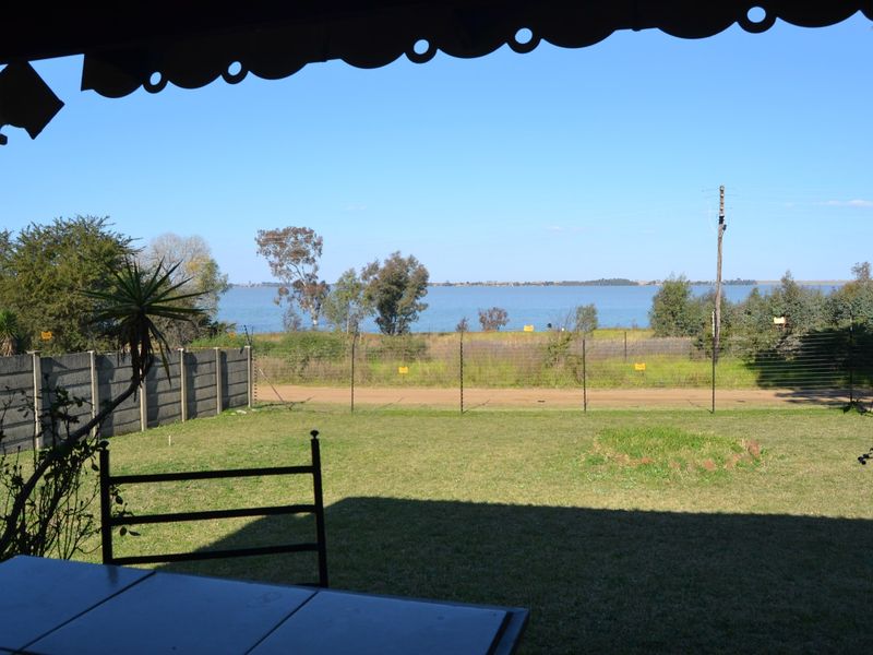 A scenic view of the lake and surrounding landscape, captured from a covered patio area with a lawn and boundary fencing.