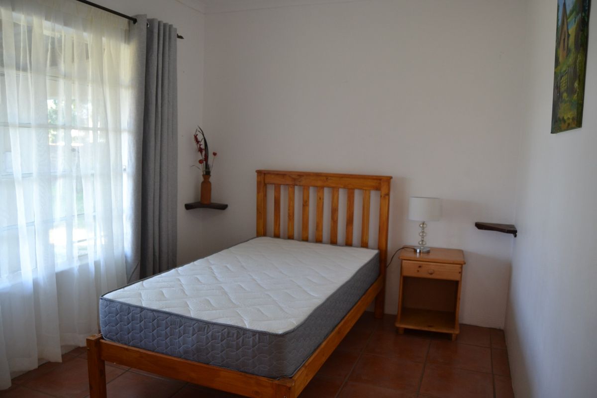 A simple bedroom featuring tiled flooring and a window with curtain rod, providing a functional and neutral space.