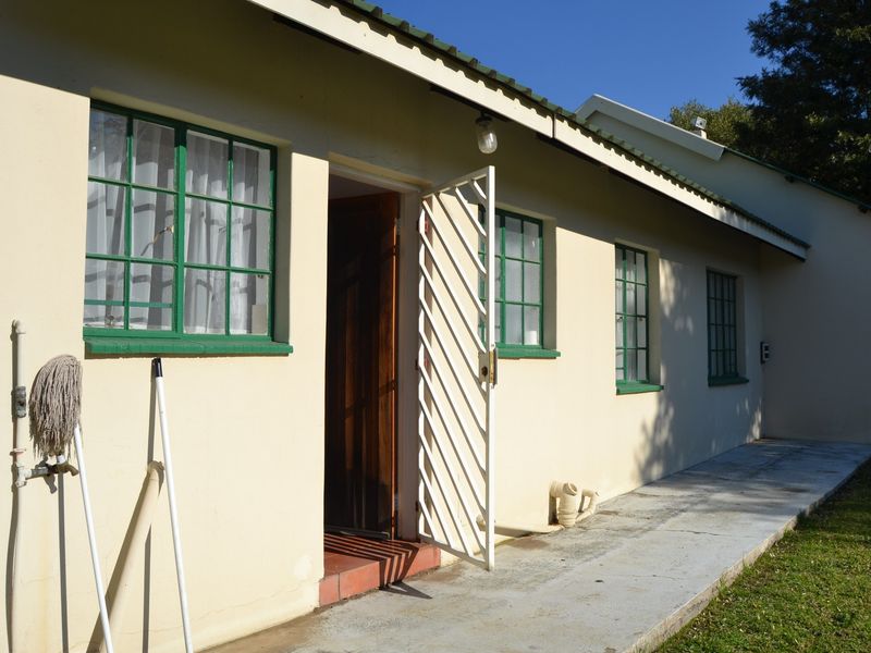 Rear exterior view of the property featuring a concrete pathway, security gate, and steel-framed windows along the building facade.