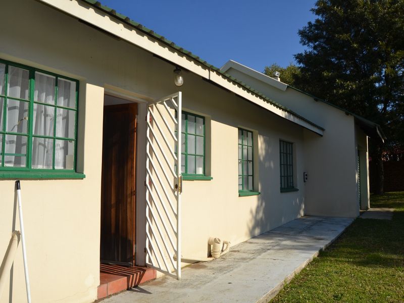 Rear exterior view of the property featuring a concrete walkway, steel-framed windows, and a metal security gate entrance.