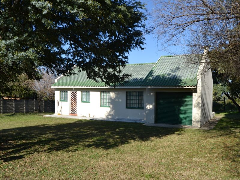 Rear view of a single-story house featuring a green corrugated metal roof, attached garage, and a spacious garden area.