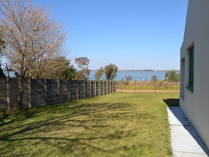 Rear garden area featuring a precast concrete boundary wall with electric fencing, a concrete pathway, and scenic water views.