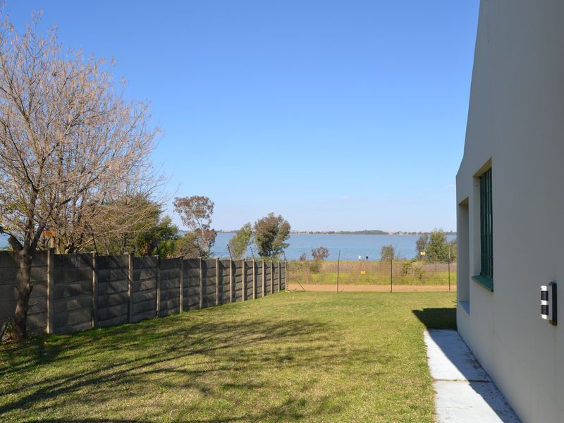 A rear garden area featuring a lawn, precast concrete boundary wall, and wire fencing with a scenic view of the water in the distance.