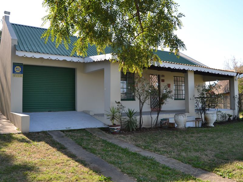 Front elevation of a single-story house featuring a green corrugated metal roof, a roller garage door, and a covered front porch.