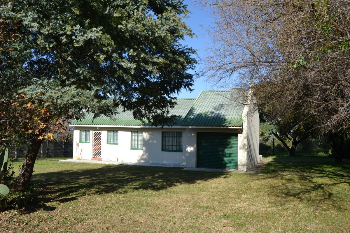 Rear view of a detached house featuring a corrugated metal roof, security gate, and integrated garage, set within a spacious garden area.