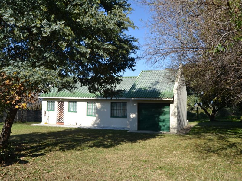 Rear view of a detached house featuring a corrugated metal roof, security gate, and integrated garage, set within a spacious garden area.