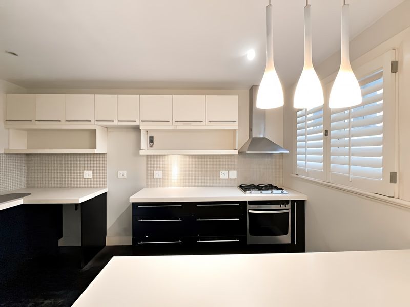 A modern kitchen featuring black lower cabinetry, white upper cabinets, mosaic tile backsplash, built-in gas cooktop, oven, and elegant pendant lighting.