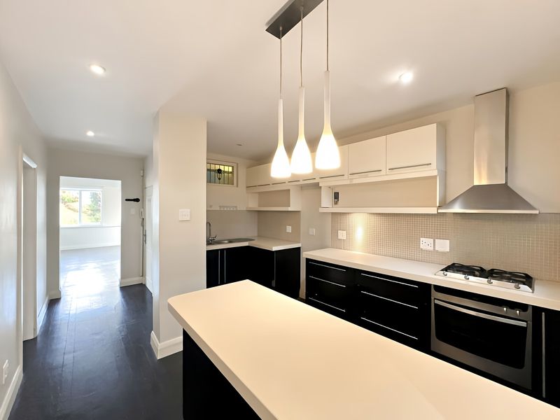 Modern kitchen featuring a central island, built-in oven, gas hob, extractor fan, and sleek cabinetry with a mosaic tile backsplash.