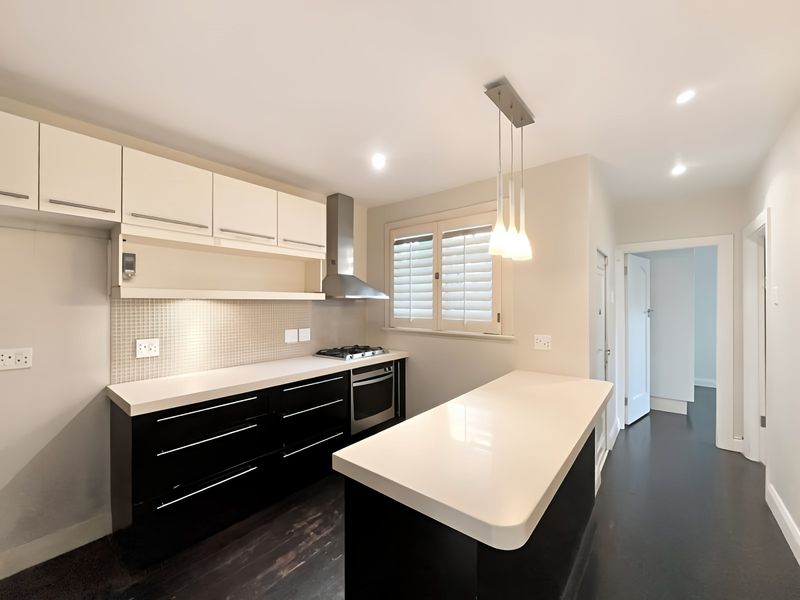 Modern kitchen featuring high-contrast black and white cabinetry, stone countertops, integrated appliances, and a functional island, finished with contemporary lighting and plantation shutters.