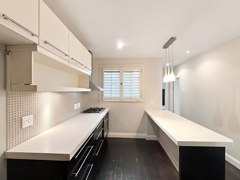 Modern kitchen featuring sleek cabinetry, a gas hob, integrated oven, mosaic backsplash, and a breakfast bar, complemented by plantation shutters and recessed lighting.