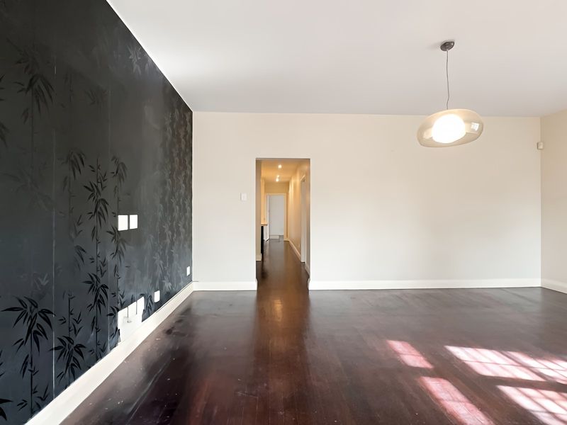 An empty living room featuring dark hardwood flooring, a distinctive bamboo-patterned accent wall, and a modern pendant light fixture.