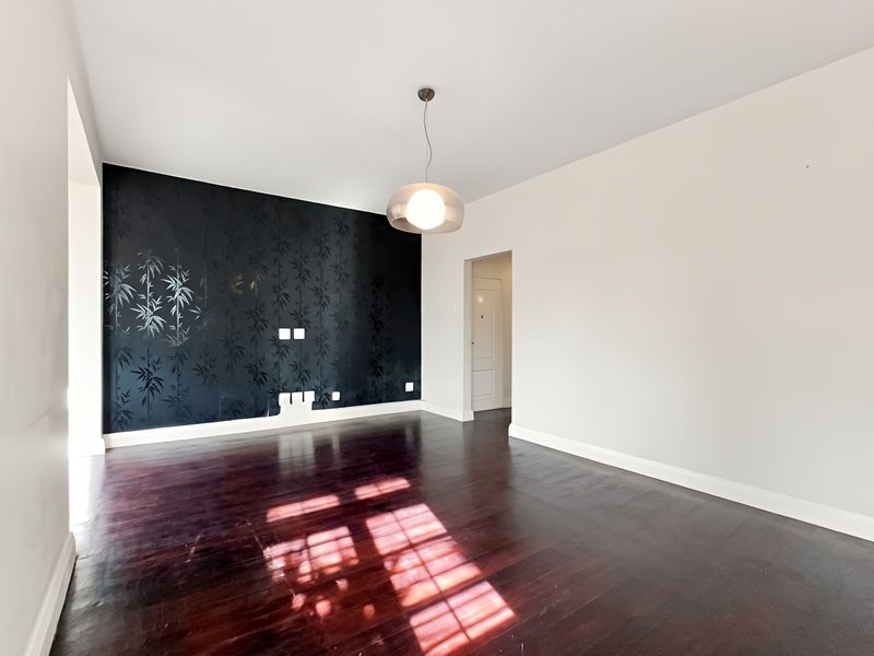 A bright, empty living room featuring dark hardwood flooring, a modern pendant light, and a striking black bamboo-patterned feature wall.