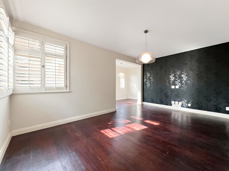 Spacious living area featuring dark hardwood flooring, plantation shutters, and a striking black feature wall with bamboo-patterned wallpaper.