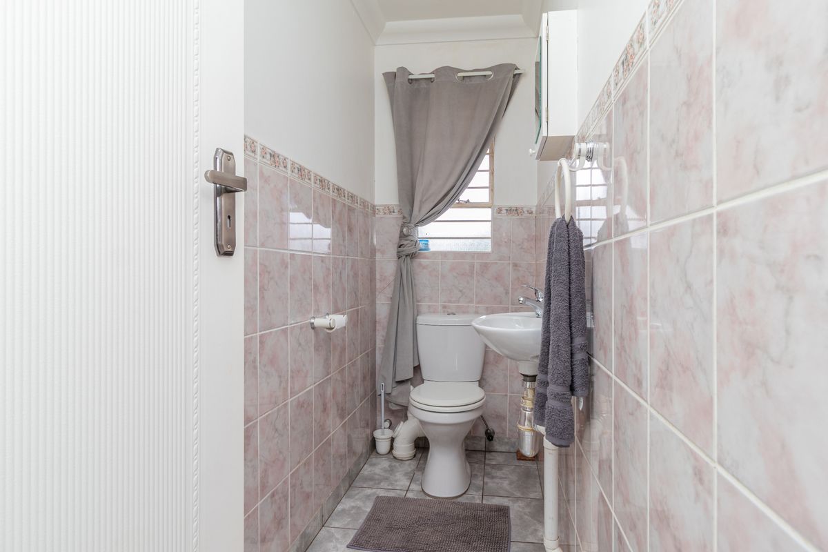 A compact guest bathroom featuring pink marble-effect wall tiles, a white pedestal basin, and a standard toilet.