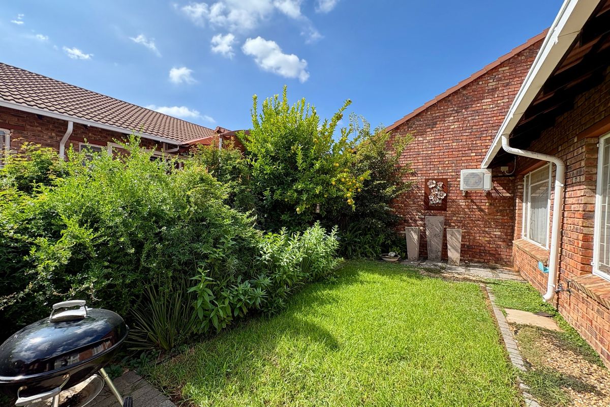 A private rear garden featuring a well-maintained lawn, brick townhouse facade, and a paved patio area.