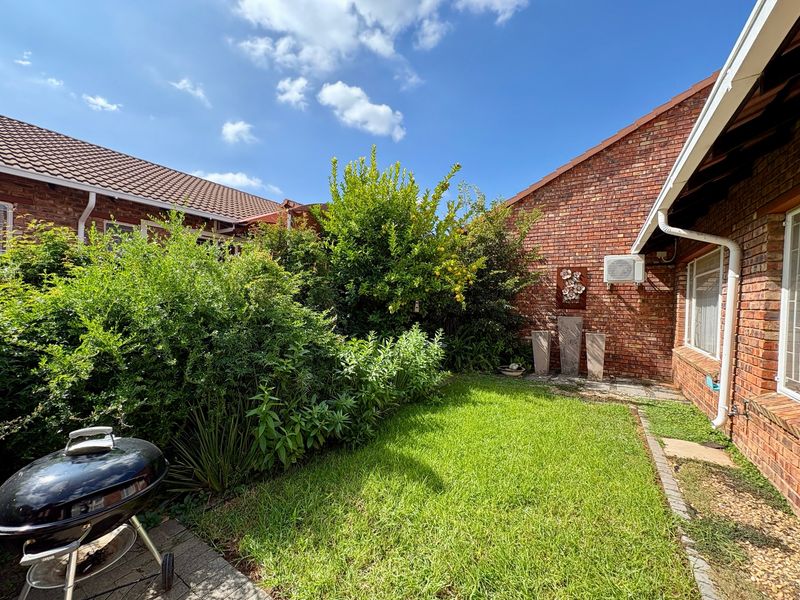 A private rear garden featuring a well-maintained lawn, brick townhouse facade, and a paved patio area.