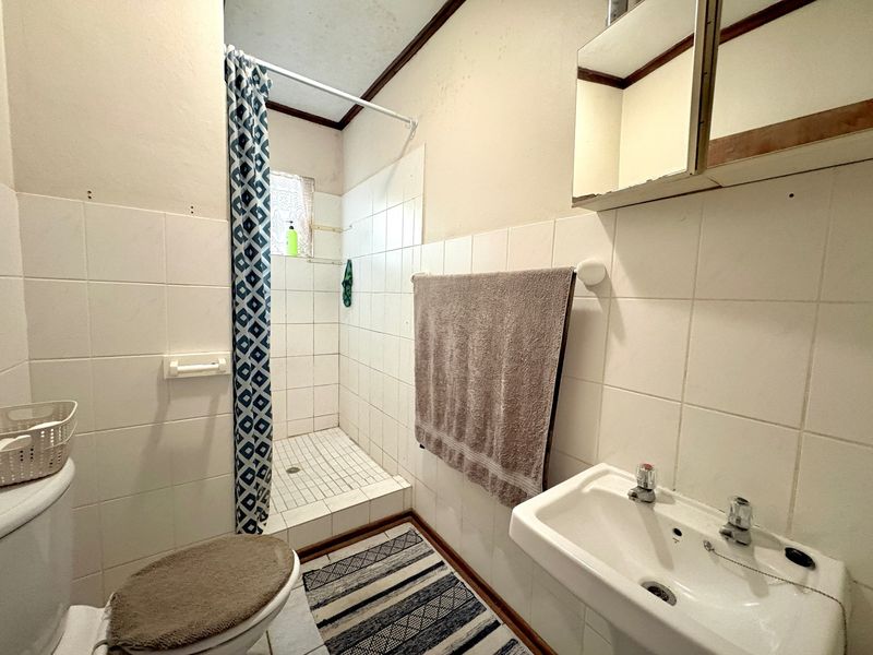A functional bathroom featuring a shower cubicle, pedestal basin, and toilet, with dated wall tiling and finishes in need of modernization.