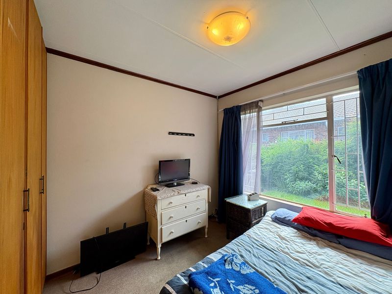 A functional bedroom featuring a built-in wardrobe, large window with garden views, and standard ceiling lighting.