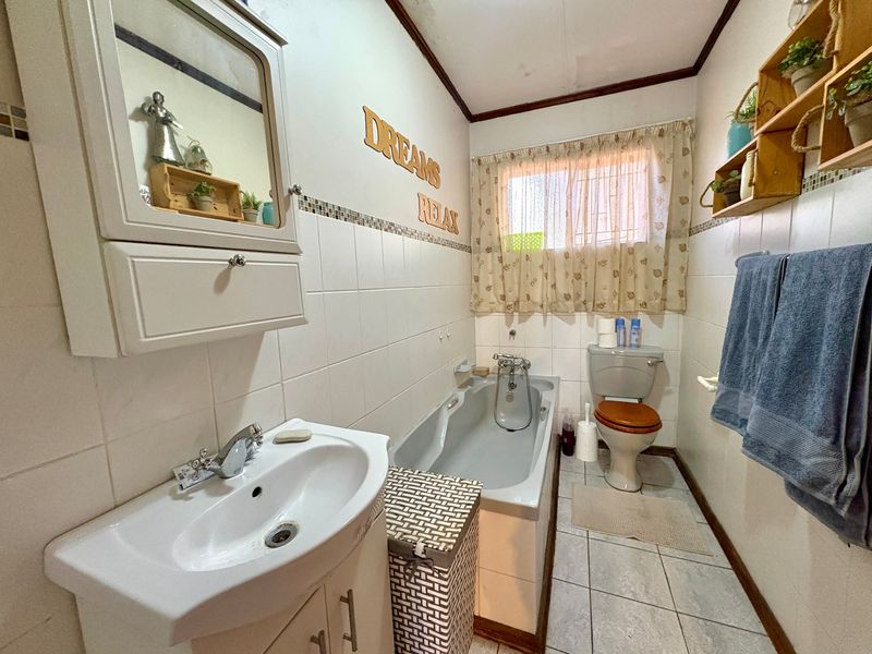 A compact bathroom featuring a bathtub, toilet, and vanity cabinet with tiled walls and flooring, showing signs of wear on the ceiling.